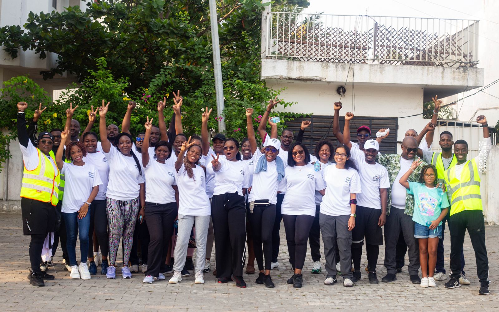 Une trentaine de membres et sympathisants des Pros de la Comm’ du Bénin, bras levés, en t-shirts blancs lors d’une activité sportive